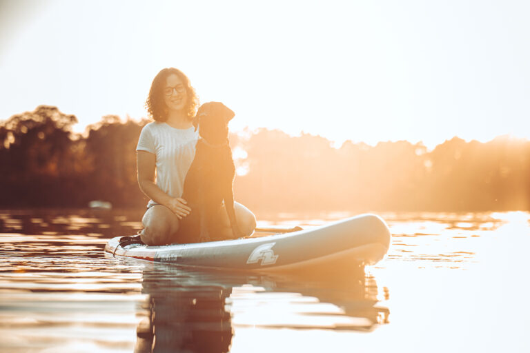 Hund und Frau sitzen auf stand up paddle in Bayern bei Pottygrafie