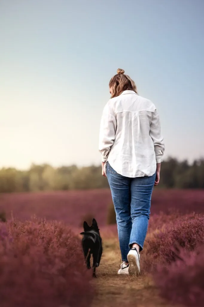 Frau läuft mit Welpe durch die Heide